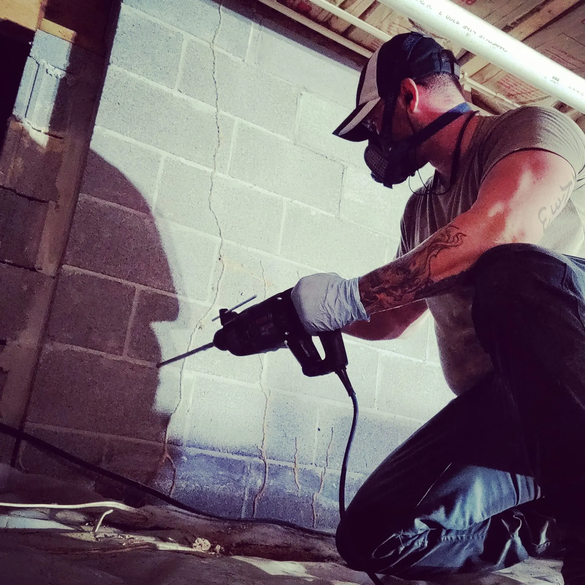 Trust Exterminating technician in a respirator drilling into a concrete block foundation wall