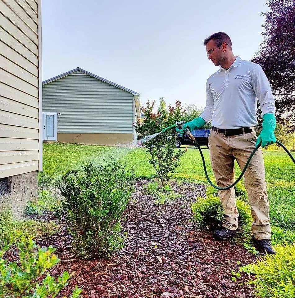 Trust Exterminating technician spraying the landscape beds beside a home